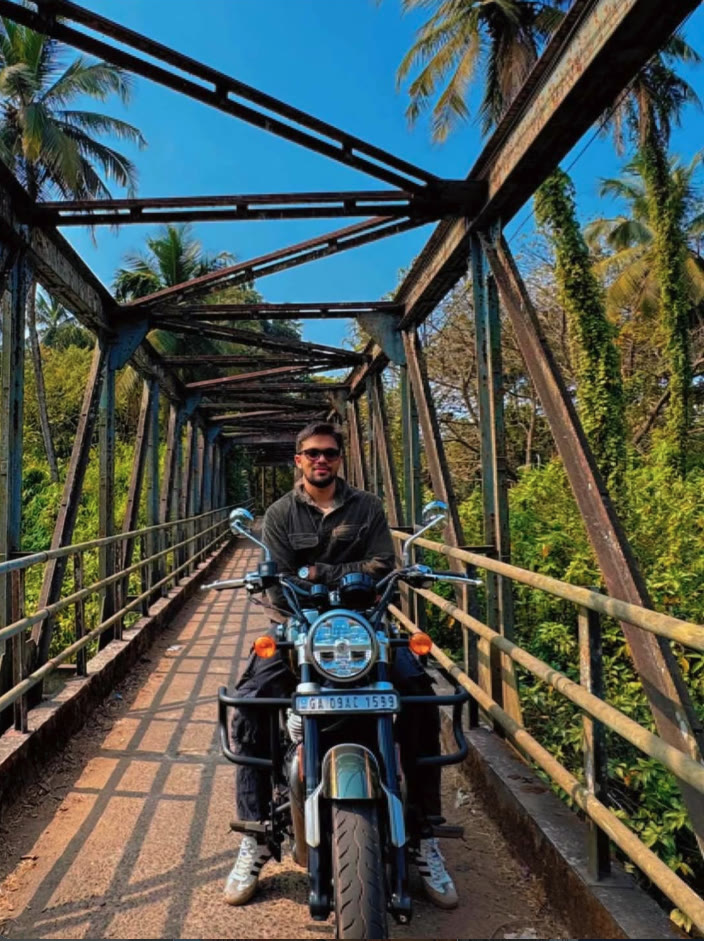 Elio on a motorbike on an old iron bridge surrounded by palm trees.