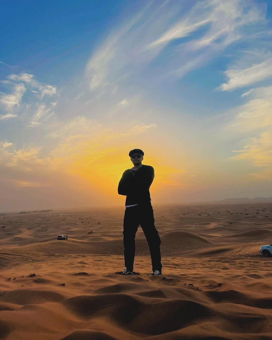 Elio silhouetted on a sand dune at sunset.